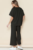 Woman wearing black casual matching sets for travel with white sneakers posing against beige background