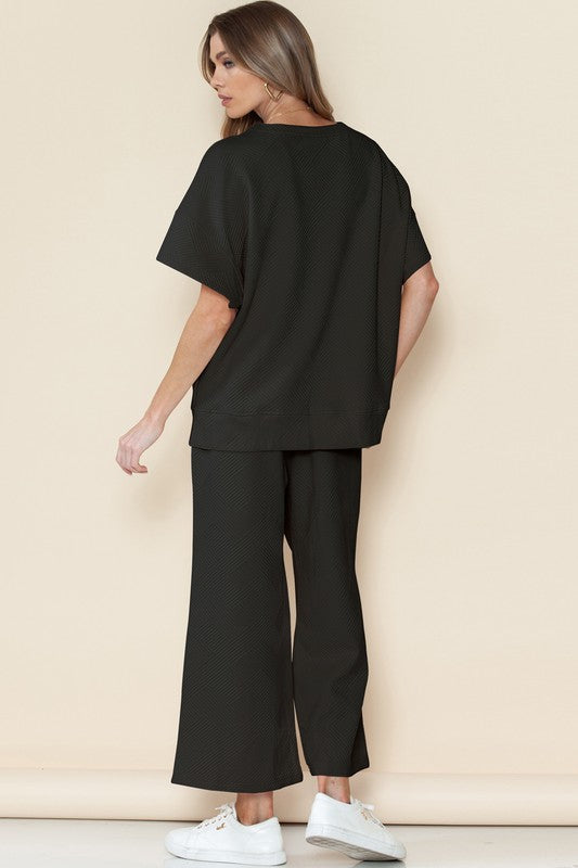 Woman wearing black casual matching sets for travel with white sneakers posing against beige background