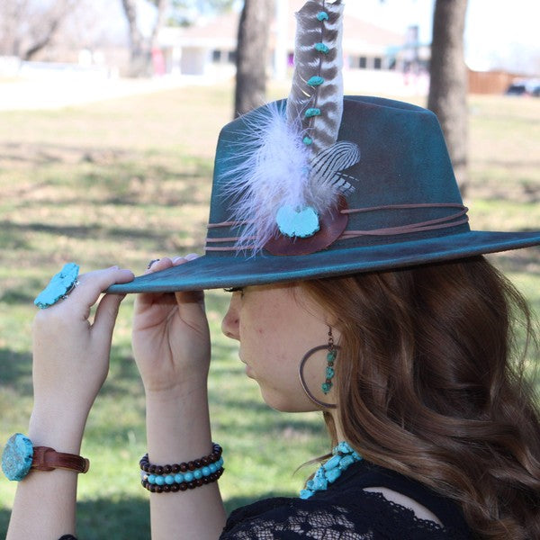 Woman wearing a stylish hat and copper hoop earrings with turquoise in a natural outdoor setting