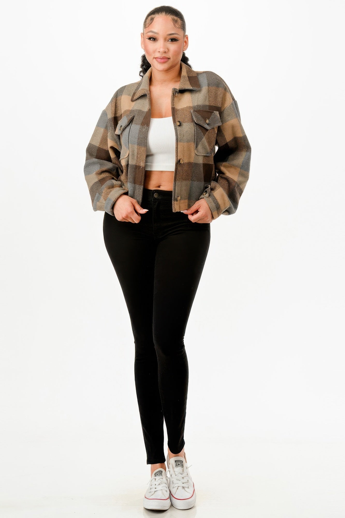 Stylish woman wearing a cropped brown flannel jacket paired with a white crop top and black skinny jeans