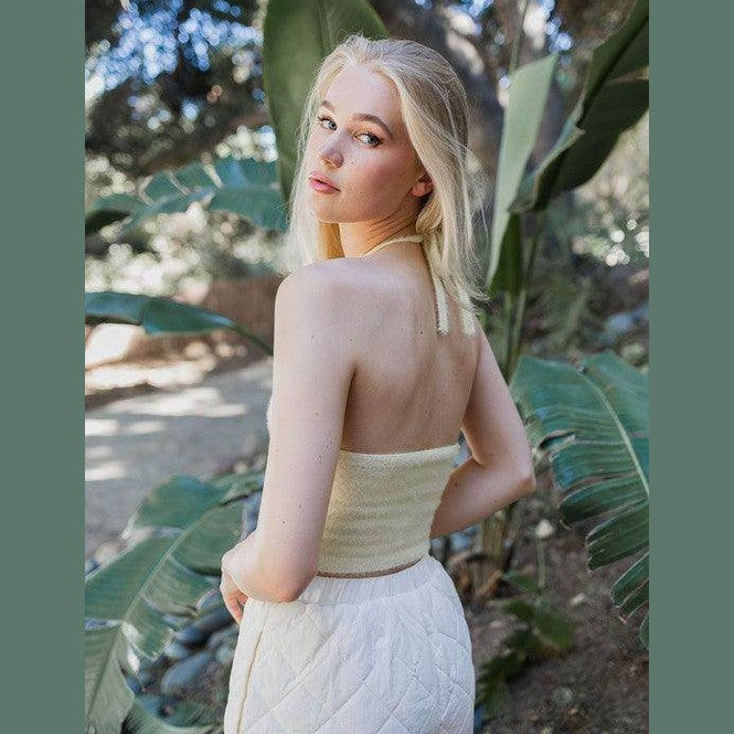 Stylish model wearing a cropped fuzzy halter top paired with a flowing skirt in a lush outdoor setting