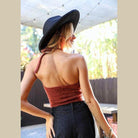 Back view of a woman wearing a cropped fuzzy halter top paired with high-waisted pants and a stylish hat