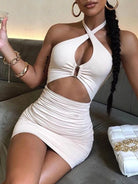 Woman wearing a white cross strap backless club dress sitting on a sofa holding a drink
