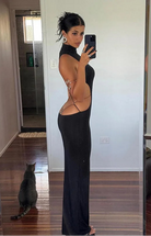 Woman wearing black backless cut out club dress taking a mirror selfie in a room with wooden floors