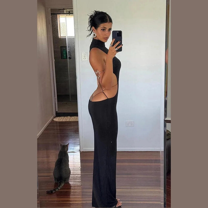 Woman wearing black backless cut out club dress taking a mirror selfie in a room with wooden floors