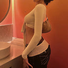 Side view of woman wearing a beige womens cropped tie front top with long sleeves and black pants