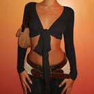 Woman wearing black womens cropped tie front top with long sleeves and v neckline styled with belt and bag