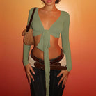 Womens cropped tie front top in sage green with long sleeves styled with dark jeans and layered belts
