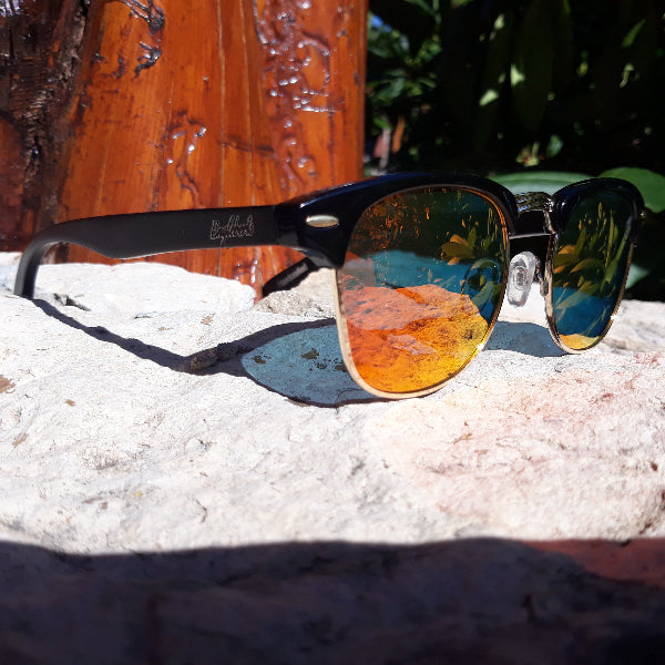 Sunglasses with reflective lenses on a rock surface with a tree stump in the background