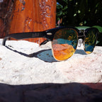 Sunglasses with reflective lenses on a rock surface with a tree stump in the background