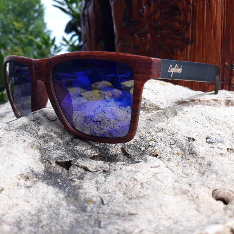 Wooden sunglasses with blue reflective lenses on a rock surface