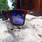 Wooden sunglasses with blue reflective lenses on a rock surface