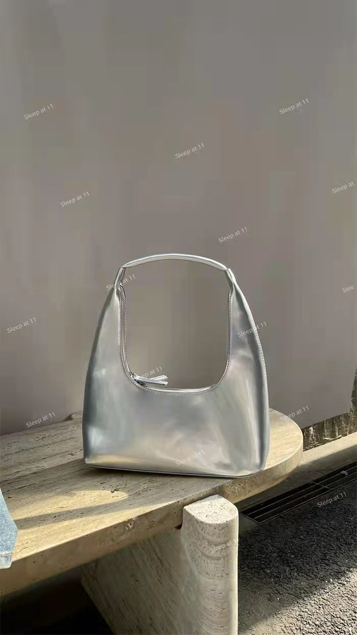 Silver Designer Retro Crescent Bag on a Wooden Table with a Minimalist Background