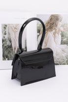 Sleek black enamel top handle crossbody bag with stylish glossy finish and elegant design