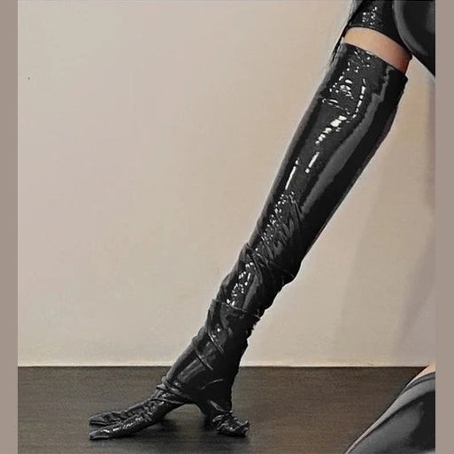 Shiny black faux leather clubwear dress thigh-high boots with pointed toes on wooden floor
