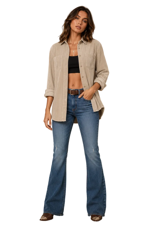 A woman models a light beige corduroy button-up shirt over a black crop top and blue flare jeans, standing against a textured beige studio backdrop.