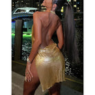 Woman wearing a shimmering gold glitter backless mini dress standing by waterfront at night