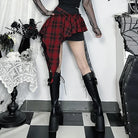Goth plaid skirt for women in red and black with asymmetrical design paired with black mesh top and knee-high boots