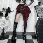 Woman wearing a goth plaid skirt for women with chains and black platform boots in a gothic room setting