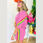 Woman wearing pink YNIQUE green colorblock lounge set with yellow and red stripes standing near flowers