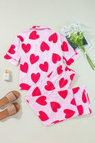 Heart print valentine pajamas set in pink with red hearts laid flat alongside slippers and flowers