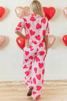 Back view of woman wearing heart print valentine pajamas set with red hearts on pink background