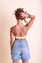 Back view of a model wearing a high neck lace top with crisscross straps and denim shorts