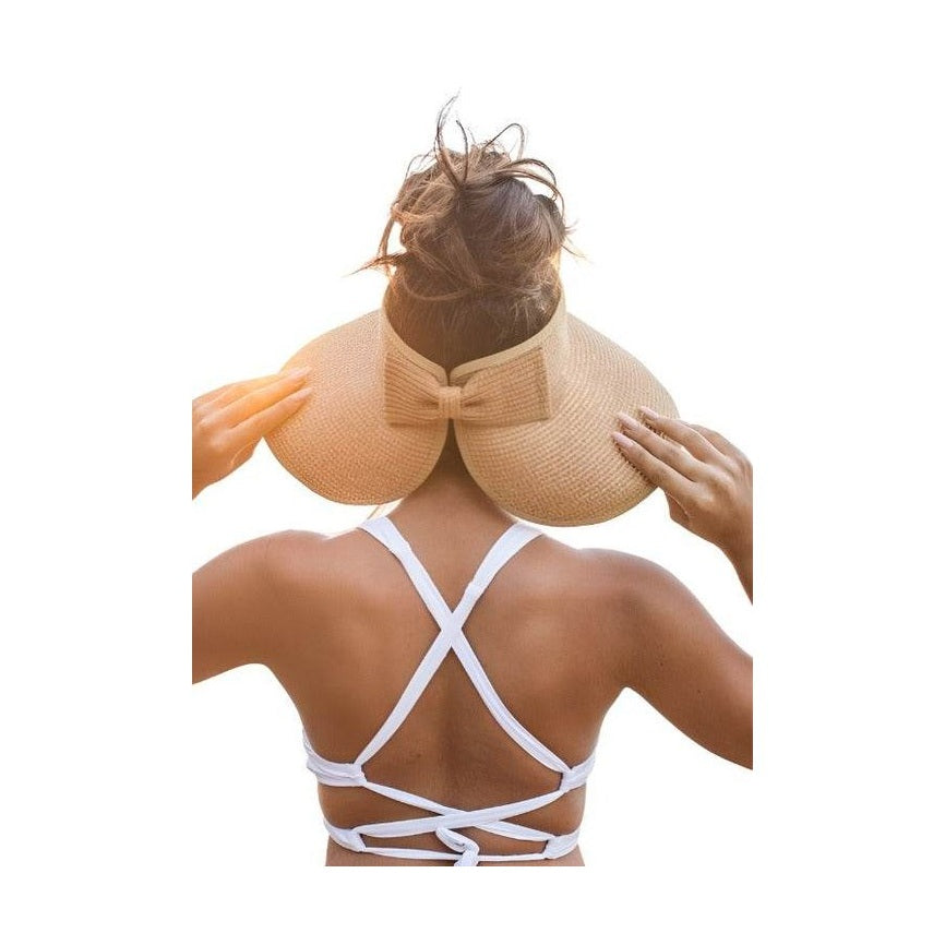 Woman wearing a large brim bow beach hat with a stylish design, perfect for sunny days at the beach.