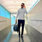 Stylish man in a gray sweater carrying a leather overnight duffel bag in a modern airport setting