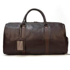 Brown leather overnight duffel bag with sturdy handles and an ID tag for travel convenience