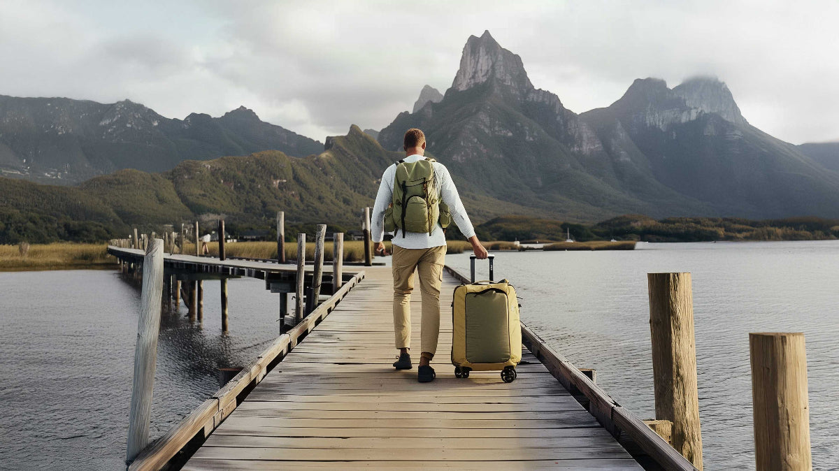 man walking down long pier with luggage on wheels and backpack on.