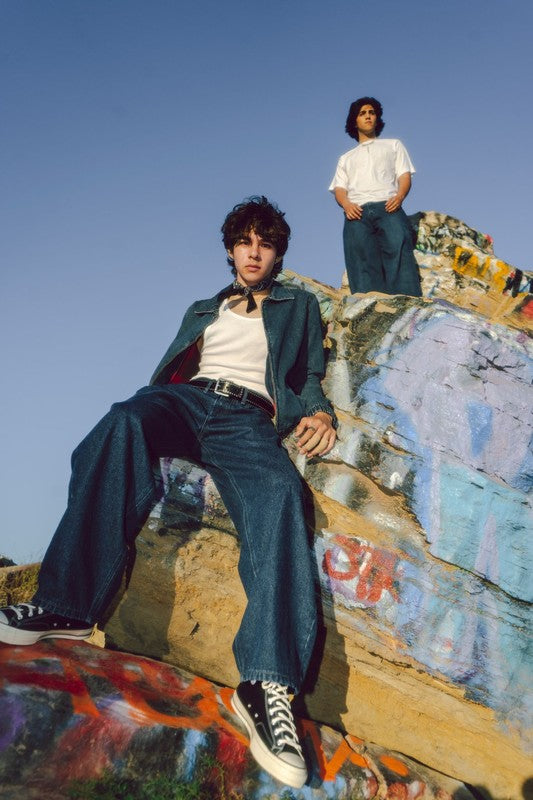 Two models wearing Generation XYZ mens baggy fit jeans posing on colorful graffiti-covered rocks under clear sky