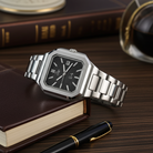 Dapr men's luxury watch with silver stainless steel band and black dial, styled on a wooden desk