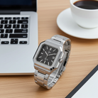 Dapr men's luxury watch with stainless steel band and black dial on a wooden desk next to a laptop and coffee