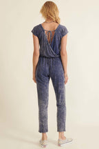 Back view of a women's mineral washed knit jumpsuit in blue with adjustable tie at the neck