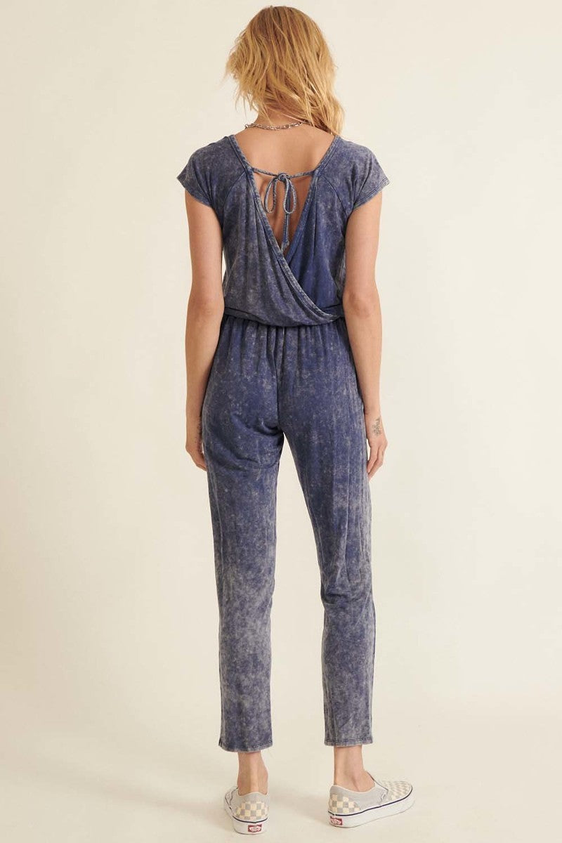 Back view of a women's mineral washed knit jumpsuit in blue with adjustable tie at the neck