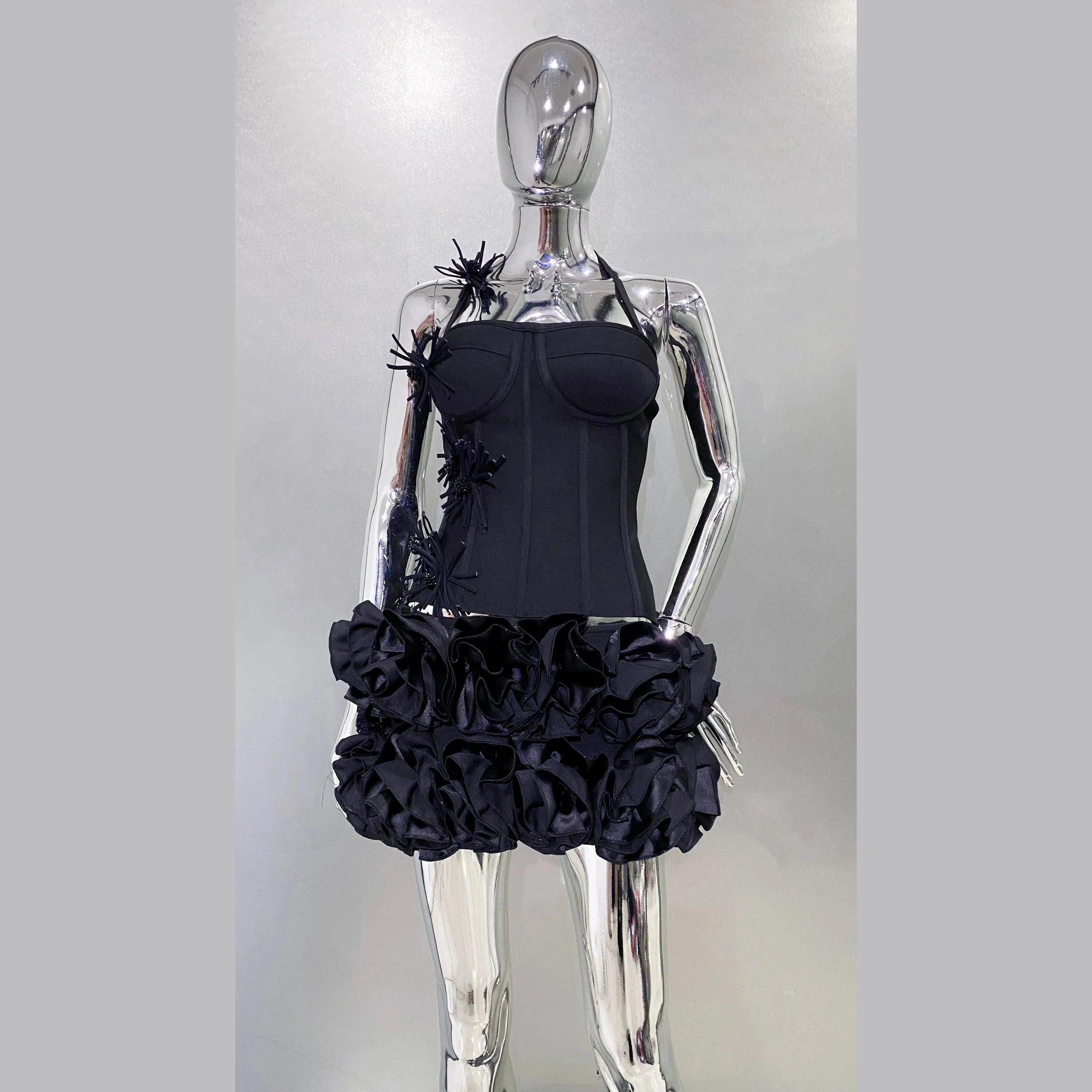 Black nightclub bandage dress for women with ruffled skirt and floral details on a silver mannequin