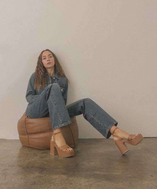 Woman wearing Norah chunky platform heels with casual denim outfit, seated on a brown pouf