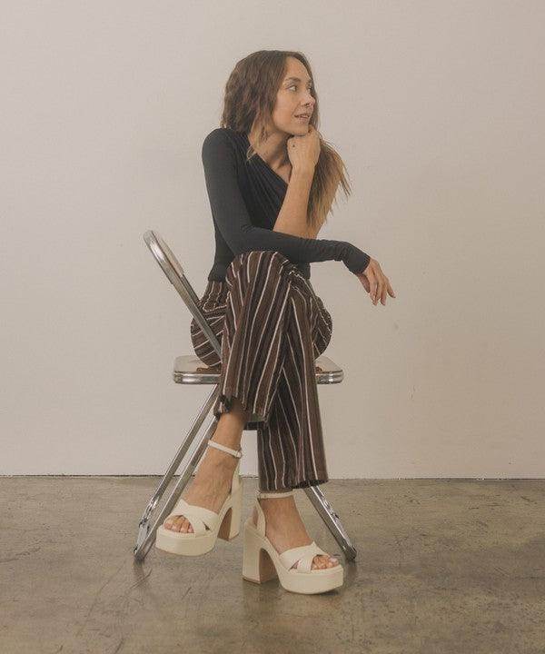 Woman sitting on a chair showcasing Norah chunky platform heels in a stylish outfit