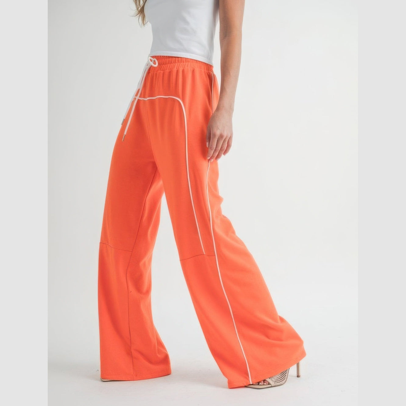 Women wearing orange drawstring pants with white piping and high heel shoes