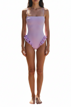 A woman wearing a light lavender one-piece swimsuit with thin shoulder straps and a ruffled hem, shown against a plain white background.