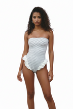 A woman modeling a strapless white bodysuit with black polka dots and a ruffled hem, paired with white leggings, against a plain white background.