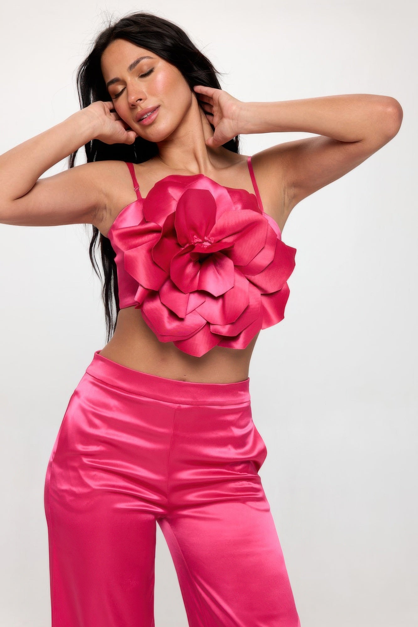 Woman wearing a pink satin crop top and wide leg pants with large floral detail on the top