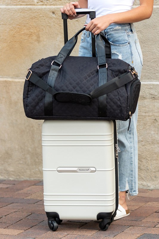Black quilted weekender bag for women stylishly attached to a white luggage suitcase