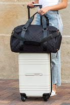 Black quilted weekender bag for women stylishly attached to a white luggage suitcase