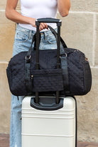 Aili's Corner quilted weekender bag for women in black with sturdy handles on a rolling suitcase