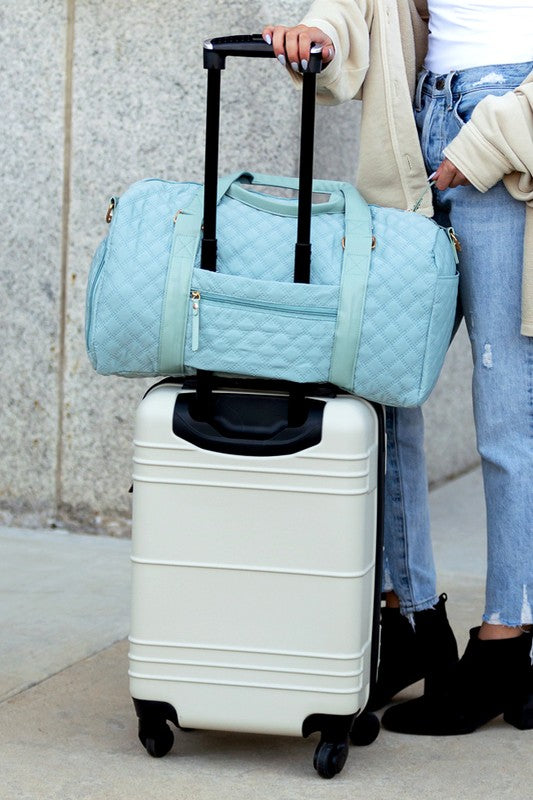 Aili's Corner quilted weekender bag for women in light blue on top of a white rolling suitcase