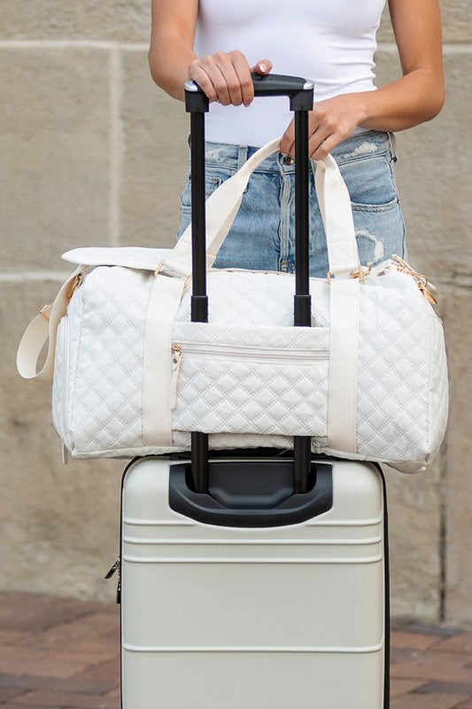 Quilted weekender bag for women in white, stylishly placed on a rolling suitcase for travel convenience