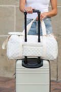 Quilted weekender bag for women in white, stylishly placed on a rolling suitcase for travel convenience