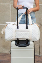 Quilted weekender bag for women in white, stylishly placed on a rolling suitcase for travel convenience
